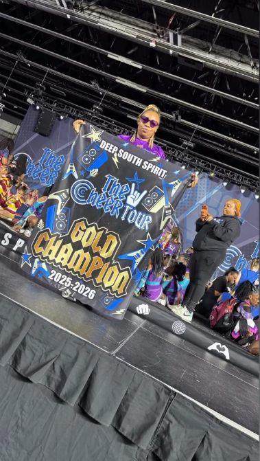A Diamond Eagles coach holding up the Gold Champion 2025-2026 banner on the competition stage